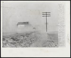 Dust Whips Across Kansas -- Two cars, one of them almost obscured, move down a road northeast of here yesterday as winds of 70 to 80 miles-an-hour whipped clouds of dust into the air in conditions reminiscent of the black blizzards of the 1930's. A barn rises above the haze but trees and telephone poles in the distance are blocked from view by the storm.