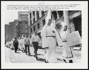 A long line of K.K.K. members and others trod down one of Atlanta’s streets here 6/6.The Klansmen carried flags and signs, this sign called for the House Un-American Activities Committee to investigate the American Civil Liberties Union.