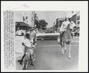 The Rider Passes--The Negro youth at left parked his steed at the curb and watched as a robed Ku Klux Klansman passes by on a hooded mount. Several hundred Klansmen and Klanswomen staged a street walk in downtown Wilson, N.C. today. Thousands of persons lined the streets to watch the walk.