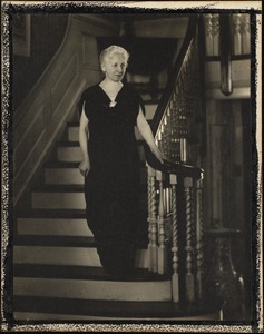 Helen Temple Cooke dressed in black velvet, pearls, and fancy brooch descending a staircase