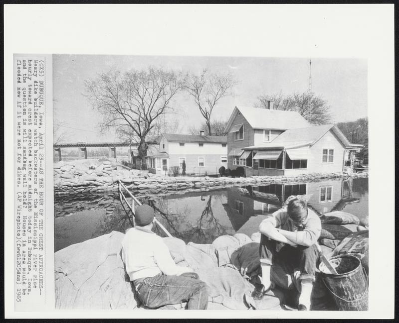 As the Hour of the Crest Approaches--Weary dike builders watch backwaters of the Mississippi river rise hourly toward crest expected before midnight today in Dubuque, Iowa, and the question is will sandbag wall hold? Houses in area would be flooded now if it were not for dikes.