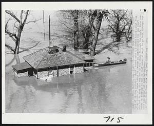 Rescued From Rooftop -- A boatload of rescue workers (right) moors onto a flooded house about five miles south of here today to rescue an unidentified man (on roof) who had to chop his way out of the place through the roof. Note over boots on rooftop as man on roof makes attempt to go back through the hole and bring out some belongings.