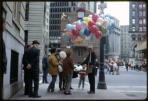 A man holding balloons with a group of people in front of the Old State House, Boston