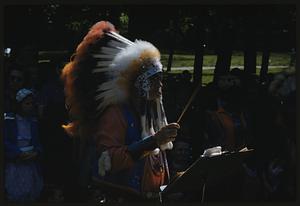 Man wearing feathered headdress conducting music