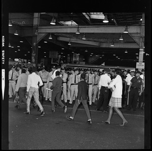 Group of students walking by uniformed officers in a bus station, possibly Dudley Square