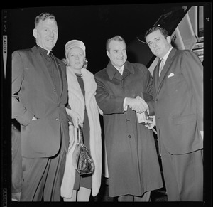 Red Skelton shaking hands with another man while his wife, Georgia Davis, a clergyman pose for the camera