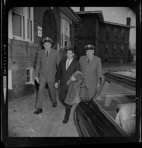 Albert DeSalvo with coat draped on arm and walking with guard Brauni Norkus, right, and one other guard on his left