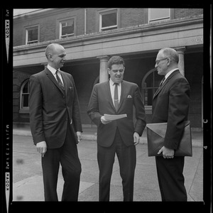 Donald Conn, assistant district attorney, flanked by two other men in suits discussing a document