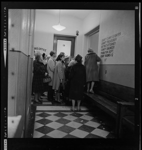 Group of people waiting in a courthouse hallway with a woman standing on a bench