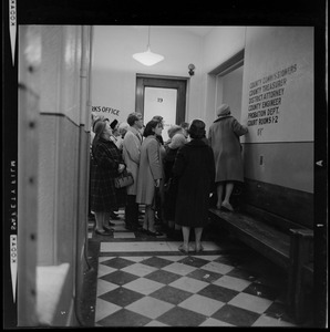 Group of people waiting in a courthouse hallway with a woman standing on a bench