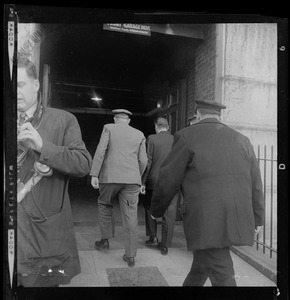 Uniformed officers walking with a man into a garage entrance