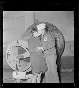 Crew member of USS Wasp carrier kissing a woman in front of spacecraft capsule