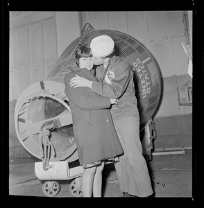 Crew member of USS Wasp carrier kissing a woman in front of spacecraft capsule