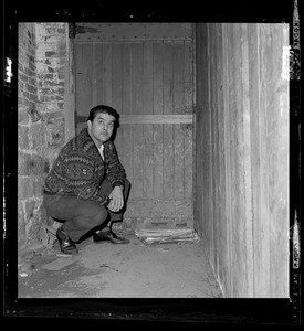 Man kneeling in a passageway by a wooden door