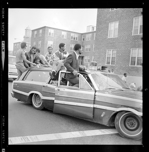 Students sitting on open doors and the roof of a station wagon