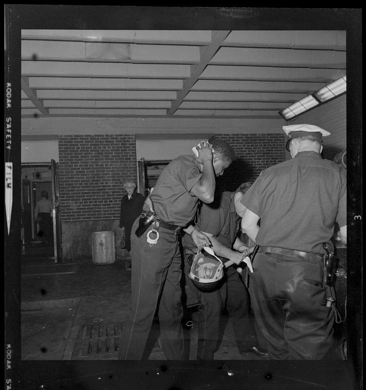 Black police officer Courtland Ballard, suffering from head injury despite the helmet he's holding in his hand, arrives at City Hospital for treatment after he was hit with a paving block