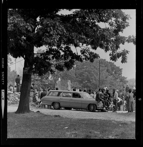 People sitting on the hood of a station wagon as a crowd gathers in Franklin Park