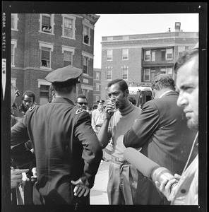 Police officer talking with an unidentified Black man who covers his mouth with a cloth, most likely near Jeremiah E. Burke High School during unrest that broke out after student demonstrations