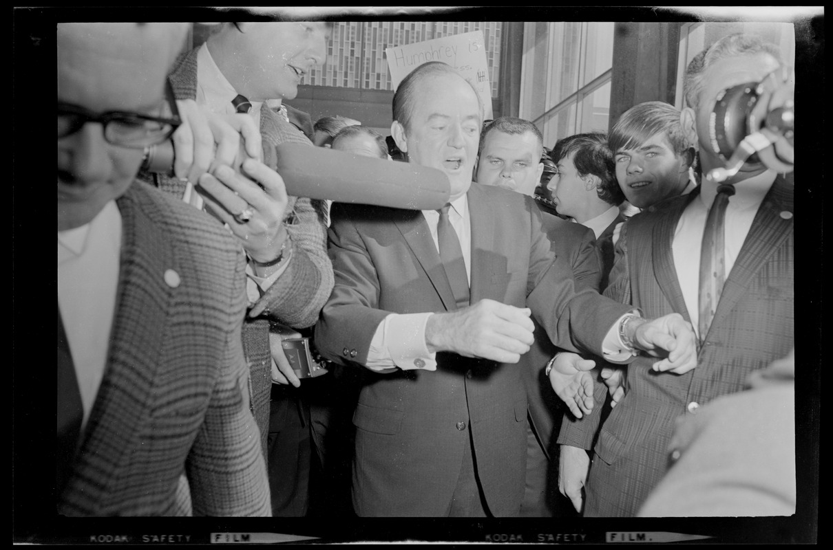 Hubert Humphrey walking through a crowd with people holding anti-Nixon and Lyndon Johnson posters