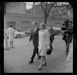 Kevin White and his wife Kathryn walking along the sidewalk, and being followed by a cameraman