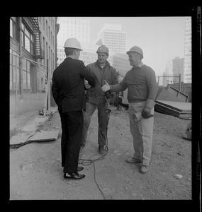 Kevin White wearing a construction hat, shakes hands with two workers