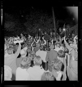 President Johnson receiving help while standing on car and surrounded by crowd
