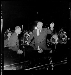 President Johnson waves to supporters while standing next to a vehicle