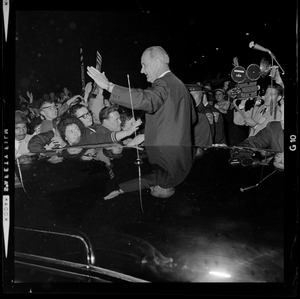 President Johnson waves to supporters while standing next to a vehicle