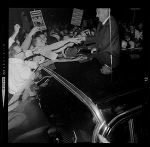President Johnson shakes hands with supporters while standing by a vehicle