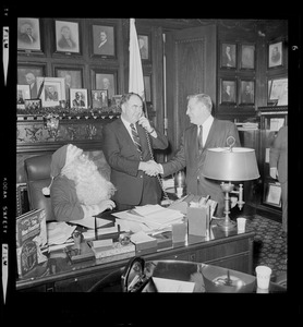 John F. X. Davoren on the phone and shaking a man's hand while a seated Santa Claus looks on