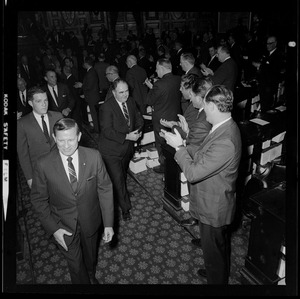 Former House Speaker John F. X. Davoren is surrounded by legislators as he walks down the aisle out of the House chamber after being named Secretary of State