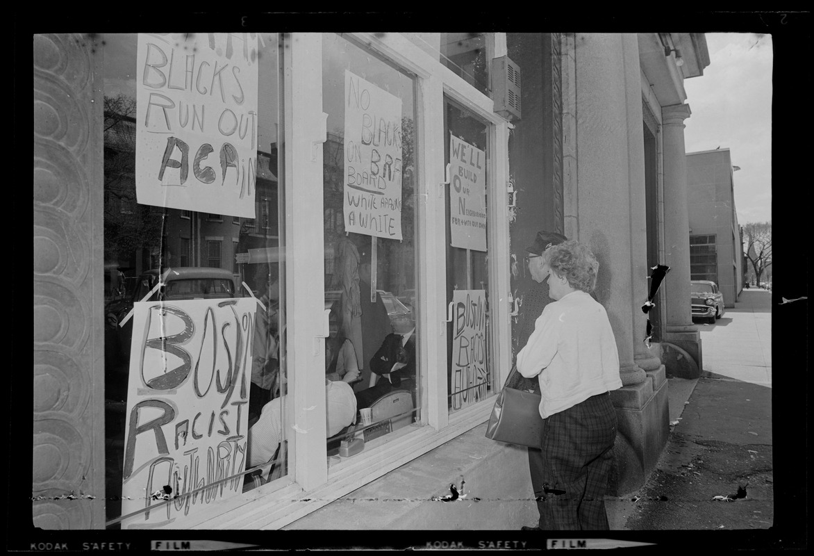 Man and woman looking at signs hanging in window of Boston Redevelopment Authority South End office