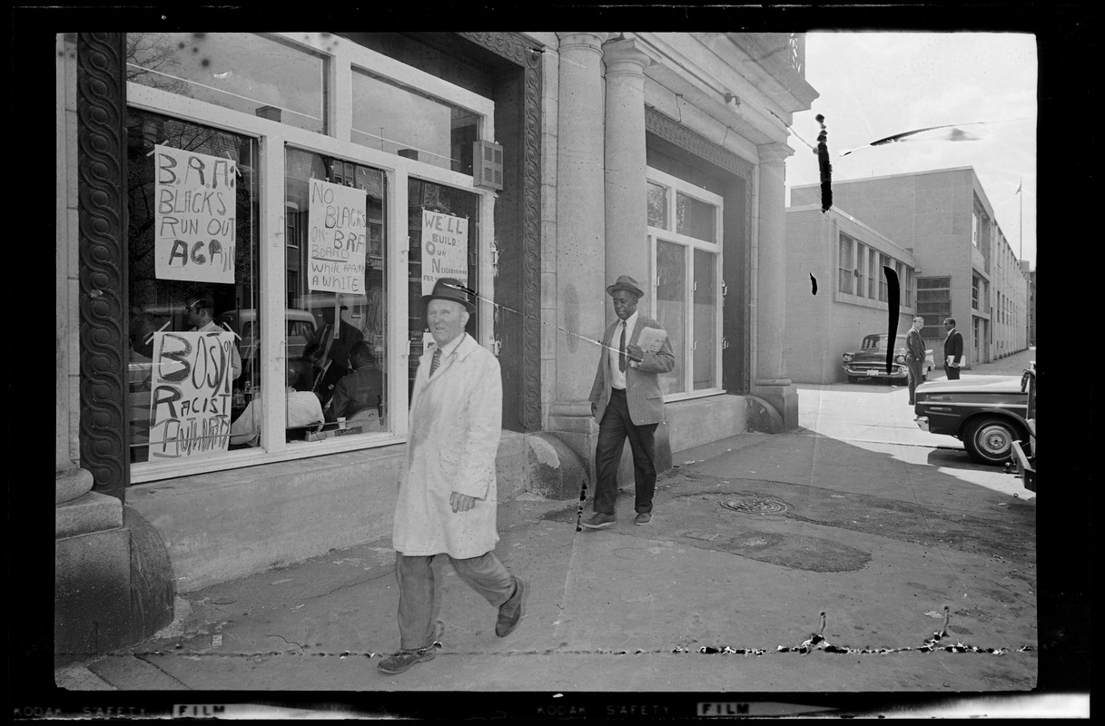 Two men walking by window of Boston Redevelopment Authority South End office