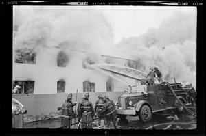 Firefighters battling a fire in a building using the hose on the engine