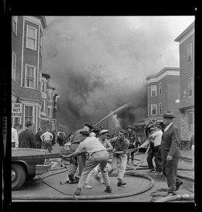 Emergency personnel and civilians working to unravel a fire hose