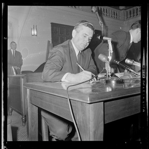 Edward J. Logue, of the Boston Redevelopment Authority, seated at desk taking notes during a Boston Redevelopment Authority hearing