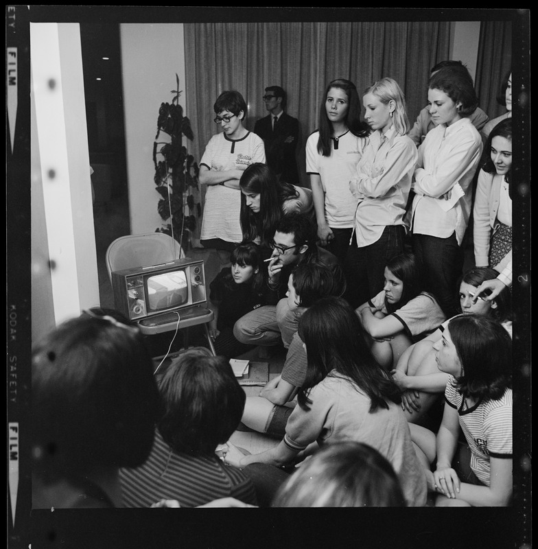 Group of women and a man gathered around a TV, most likely broadcasting information about the BU sit-in