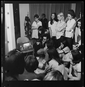 Group of women and a man gathered around a TV, most likely broadcasting information about the BU sit-in