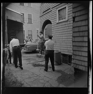 Police officers watching a man carrying a lamp out of a building