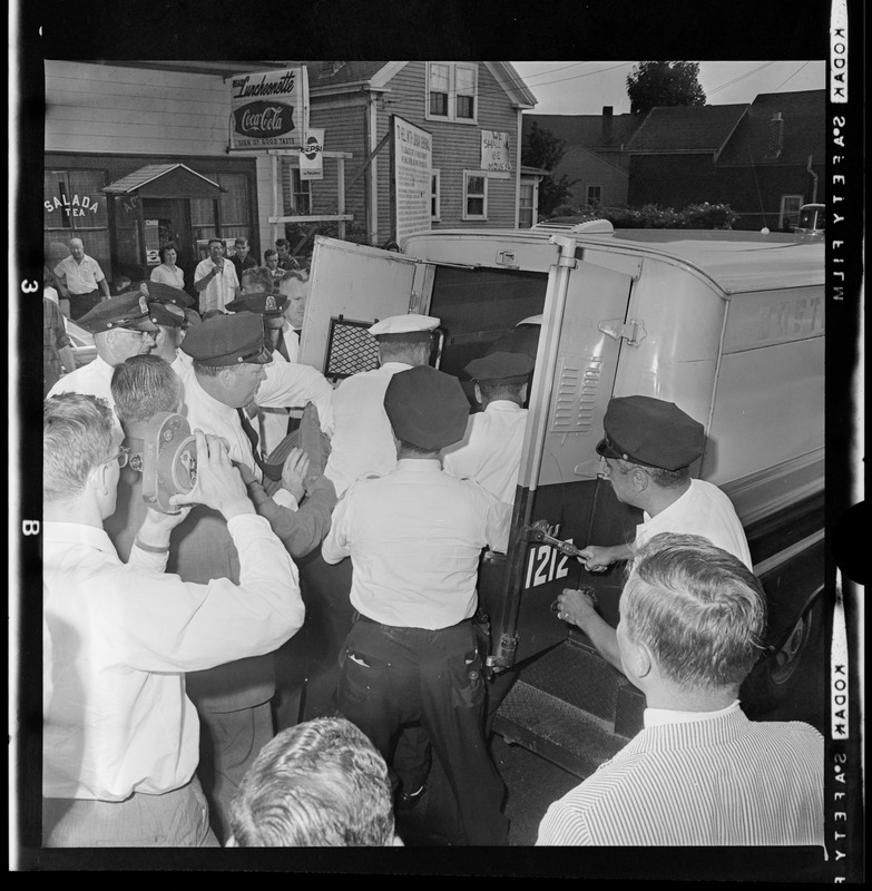 Police officers putting a person in the back of a police department wagon