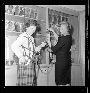 Marjorie Brown holding a horse bridle while her mother, Marjorie, places an award in the trophy case