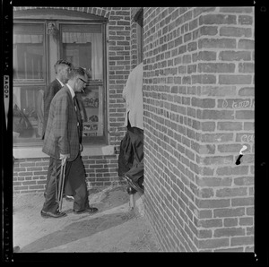 Men walking inside of building, one has a cigarette and rifle in hand