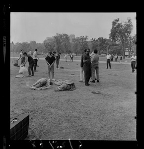 Man prodding two people laying in the grass on the Boston Common