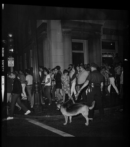 Policeman with a dog watching a crowd move on the sidewalk