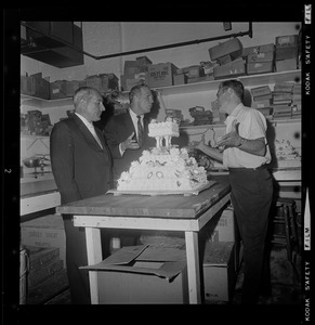 Mayor Kevin White and another man standing around and discussing a cake with another man