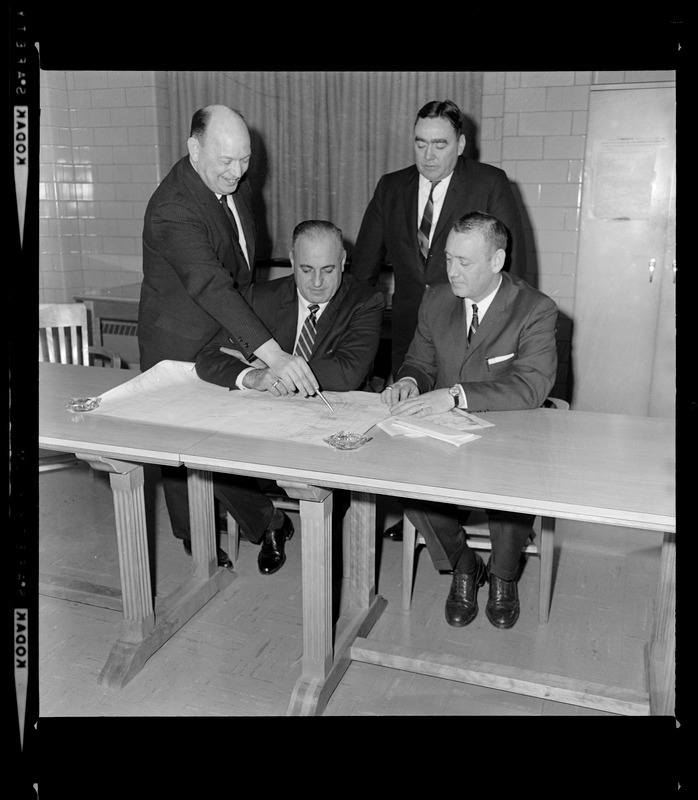 Captain Edw. F. Fahey of the MDC points to map of roadway of new pike--soon to open to the Northeast Expressway to Capt. Peter Bille of MDC (Old Colony Div), Capt Mike Faherty of the State police (seated right), and standing in the background is Boston Police Deputy Superintendent James Buchanan