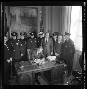 Mayor Kevin White at his desk signing Boston Police salary bill with officers behind him