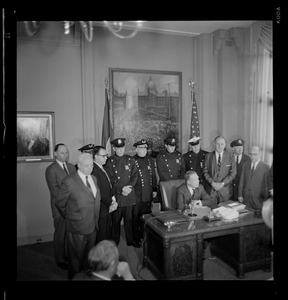 Mayor Kevin White at his desk signing Boston Police salary bill with officers behind him