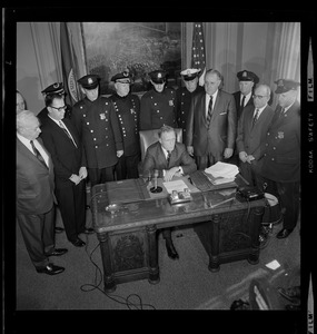 Mayor Kevin White at his desk signing Boston Police salary bill with officers behind him