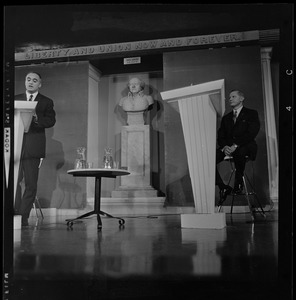 Lt. Gov. Francis X. Bellotti speaking at the podium and former Gov. Volpe, seated on stage, during the debate